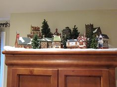 a christmas scene with houses and trees on top of a dresser in the living room