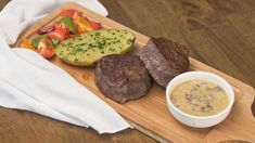 steak, potatoes and vegetables on a cutting board next to a bowl of dip sauce