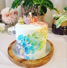 a colorful cake with flowers and candles on it sitting on a table next to potted plants