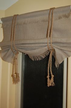 a window curtain with rope hanging from it's side and an open door in the background