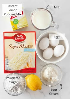 ingredients to make lemon cake laid out on a white marble counter top, including eggs, flour, butter and sugar