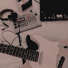 an electric guitar, headphones, and other musical equipment sit on a white sheet