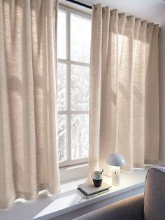 a window with curtains and a lamp on the ledge in front of it, next to a couch