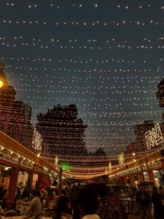 many people are walking through an indoor shopping mall with lights strung from the ceiling above them