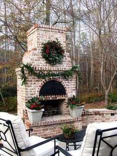 an outdoor fireplace with potted plants and wreaths on it, surrounded by patio furniture