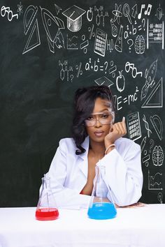 a woman sitting at a table in front of a chalkboard with science symbols on it