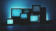 an assortment of televisions sitting on top of each other in front of a blue light