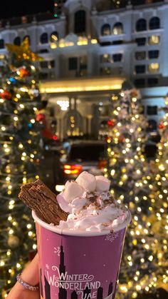 a person holding up a cup with ice cream and cookies on it in front of a christmas tree