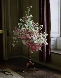 a vase filled with white and pink flowers sitting on top of a wooden tripod