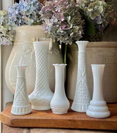 four white vases sitting on top of a wooden table next to purple and blue flowers