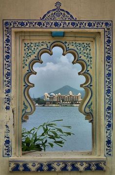 an ornate window frame with a view of a lake and mountains in the distance, framed by blue and white tiles