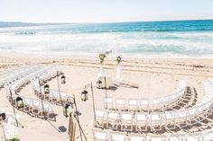 an outdoor wedding setup on the beach with white chairs and floral centerpieces set up