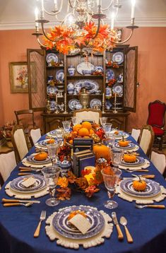 a dining room table is set with blue and white plates, silverware, and pumpkins