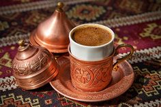 there is a cup of coffee on the saucer and two copper cups are next to each other