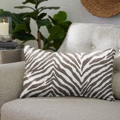 a zebra print pillow sitting on top of a gray couch next to a green plant