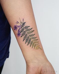 a woman's arm with a flower and fern tattoo on the left side of her arm