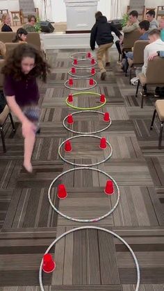 a woman is jumping over rows of red cups on the floor in a room full of people