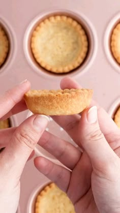 a person holding a pastry in front of muffin tins filled with mini pies