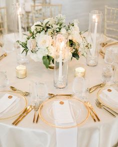 the table is set with white flowers and gold place settings for dinner guests to enjoy