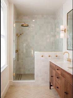 a bathroom with a walk in shower next to a white sink and wooden cabinetry