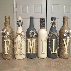 four wine bottles are decorated with flowers and the word family is spelled out in front of them