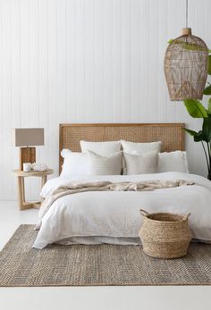 a bed with white linens and pillows in a bedroom next to a potted plant