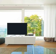 a flat screen tv sitting on top of a white table in front of a window