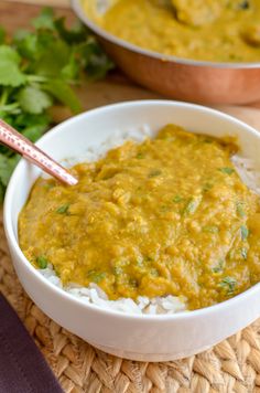 a bowl filled with rice and curry next to another bowl full of green vegetables on the side