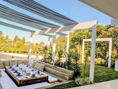 an outdoor seating area with tables and chairs on the grass, under a pergolated roof