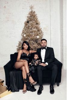 a man and woman sitting on a couch next to a small child in front of a christmas tree