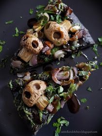 two slices of pizza with mushrooms, onions and greens on a black plate topped with parsley