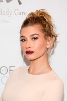 a close up of a person with a hair bun and lipstick on her face, wearing a white top