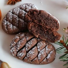 three chocolate cookies on a white plate next to an orange and cinnamon sprig