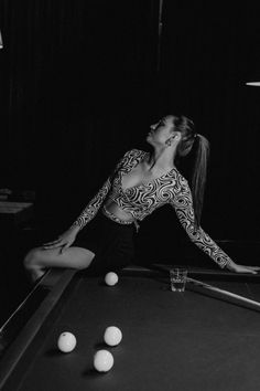 a woman sitting on top of a pool table next to a pool ball racket