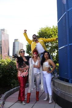 three women and one man posing in front of a blue building with their arms up