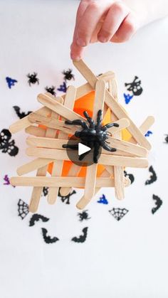 a person holding a wooden stick with a black spider on it and an orange ball in the center