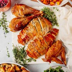 two turkeys on a platter surrounded by other thanksgiving foods and garnished with fresh herbs