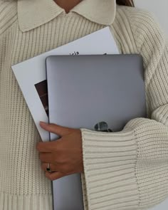 a woman in a sweater holding a laptop computer with her hands on the back of it