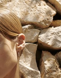 a close up of a person wearing earring next to rock wall with rocks in the background