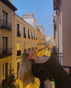 a woman is looking up into the sky while standing on a balcony with buildings in the background