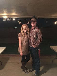 a man and woman standing next to each other in front of a deer antler