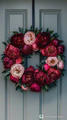 a wreath made out of flowers on the front door with green leaves and pink peonies