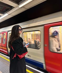 a woman is standing on the platform looking at her cell phone while waiting for the train