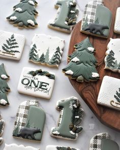 decorated cookies with trees and the number one are on a wooden platter next to other cookies