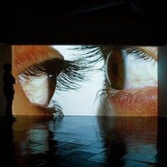 a person standing in front of a large screen with an image of two eyes on it