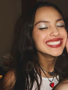 a young woman smiles as she holds her hand up to her face while wearing a necklace