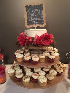 a three tiered cake with cupcakes and candy on the bottom is decorated with red flowers