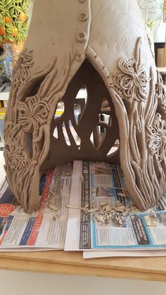 a clay house sitting on top of a table next to some newspapers and flowers in the background