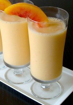 two glasses filled with orange juice sitting on top of a white tray next to each other