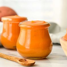 three small jars filled with orange colored liquid and wooden spoons next to each other